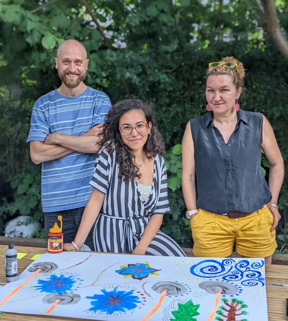 The canopy team, which is three people, sitting and standing outside in a garden on a sunny day.